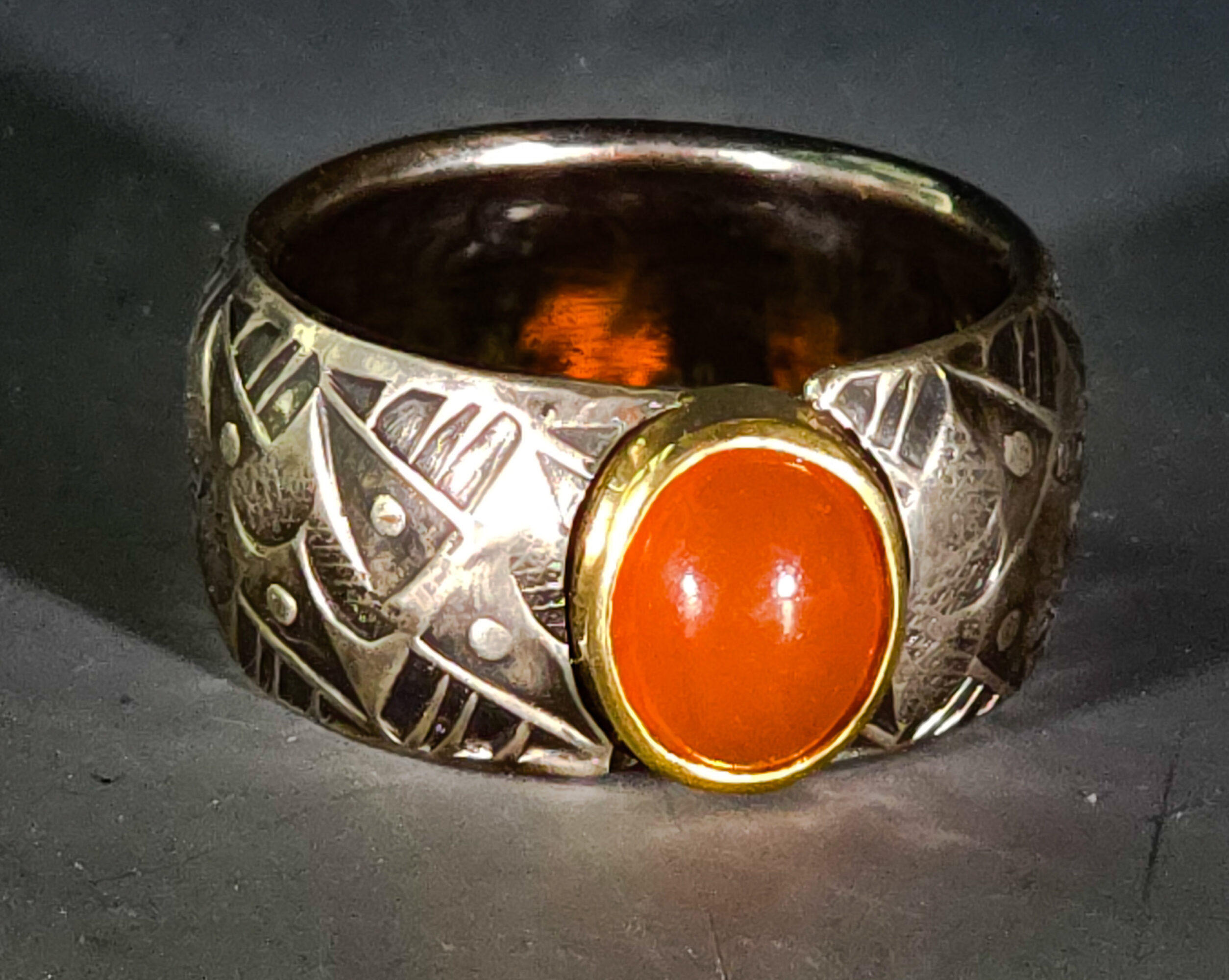 Ring with intricate patterns and a large orange oval stone set in a gold bezel.