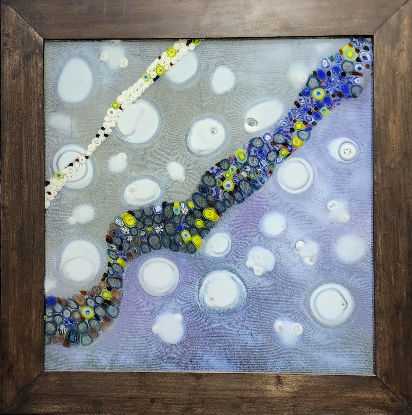 Abstract artwork with colorful circular patterns and white bubbles on a blue background, framed in wood.