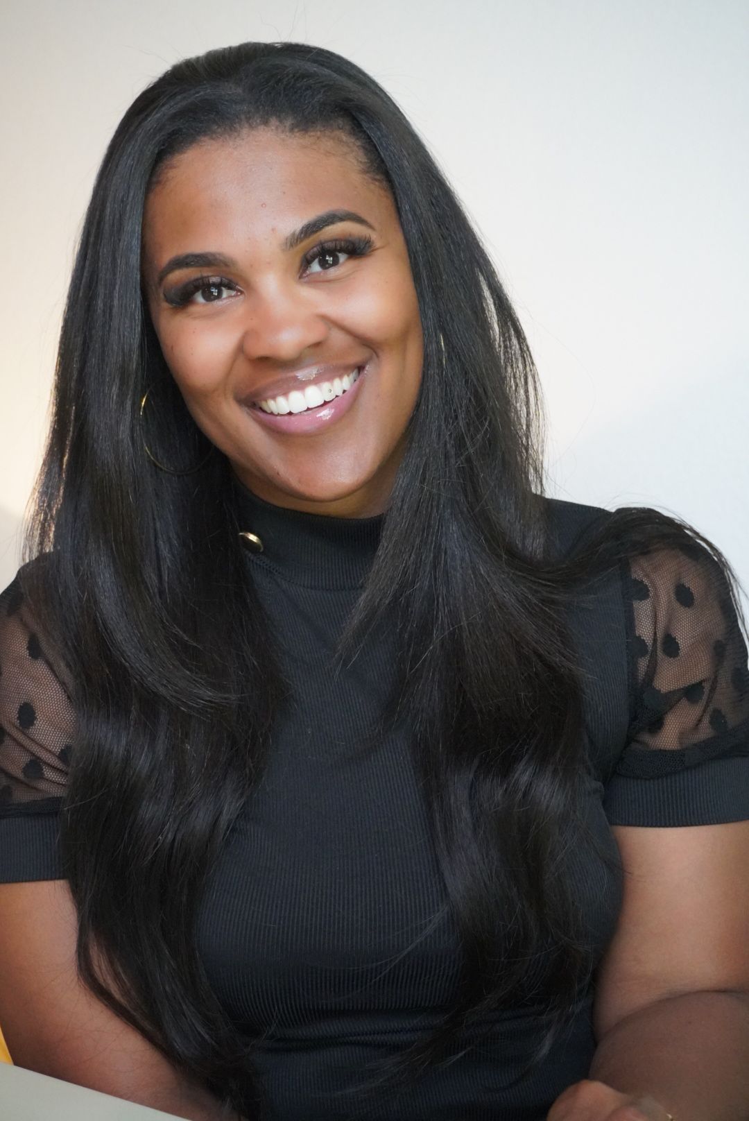 Smiling woman with long black hair wearing a black top with sheer polka-dot sleeves.