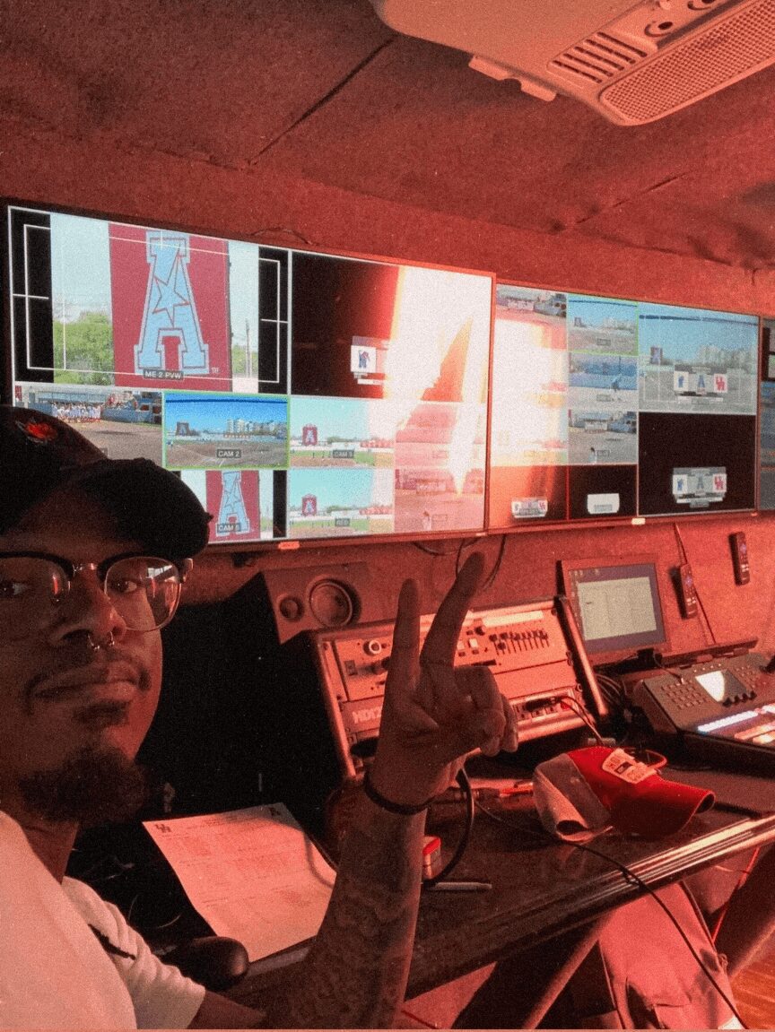 Person taking a selfie in front of multiple screens displaying technical and graphical data, making a peace sign gesture.