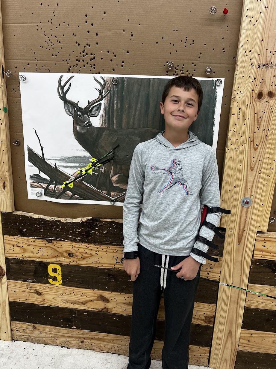 Boy standing in front of a nature-themed display with a deer and a dragonfly, smiling, wearing a gray hoodie and dark pants.