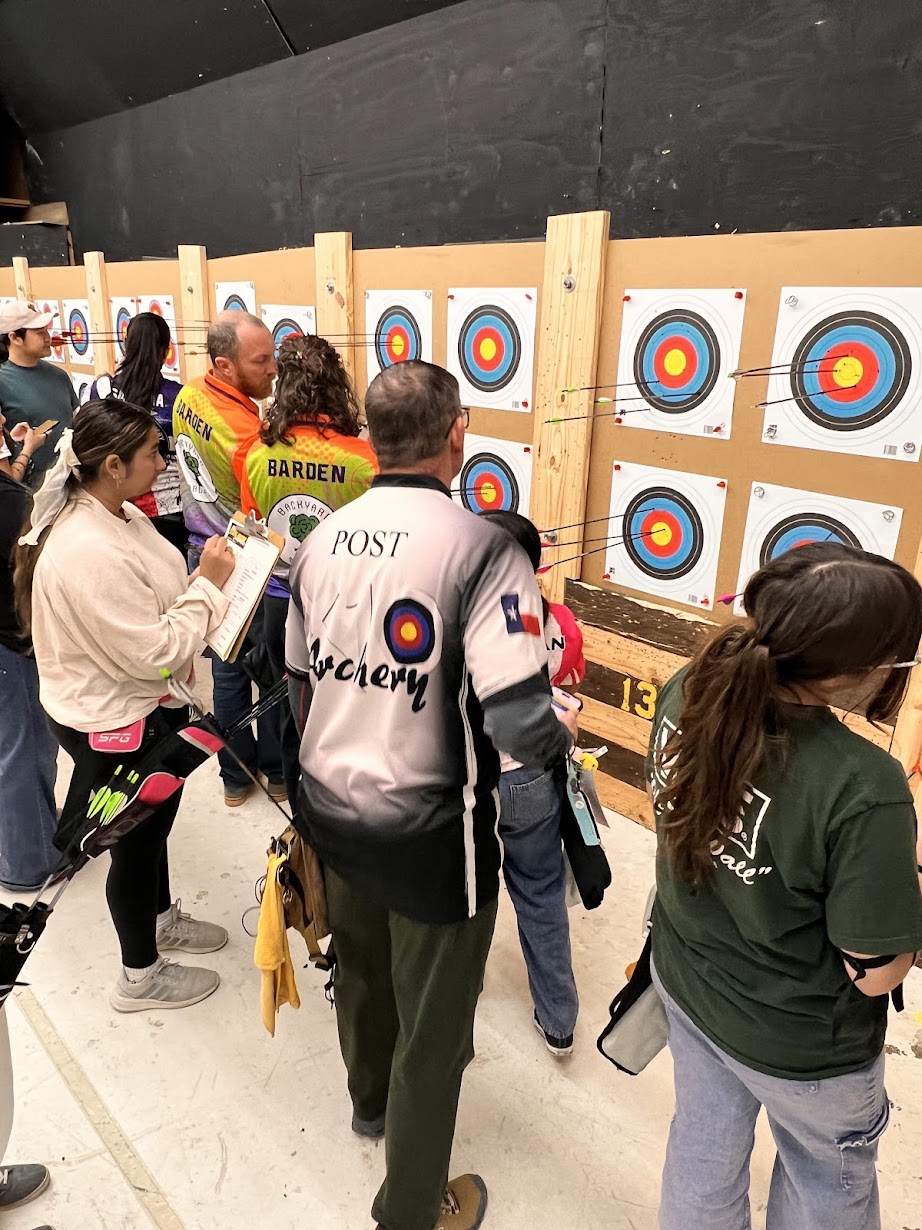 Group of people observing archery targets displayed on wooden panels at an indoor range.