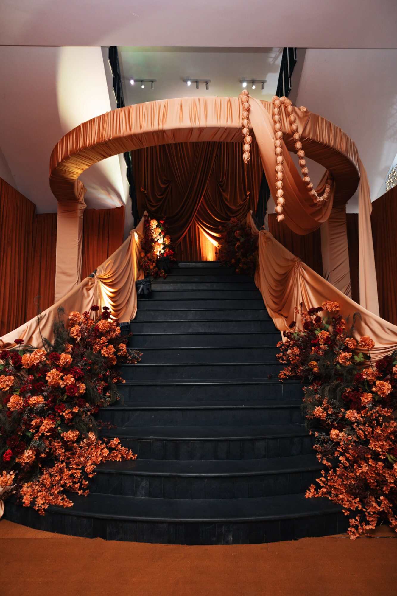 Black staircase with floral arrangements on sides, leading to a decorated stage with drapes and warm lighting.