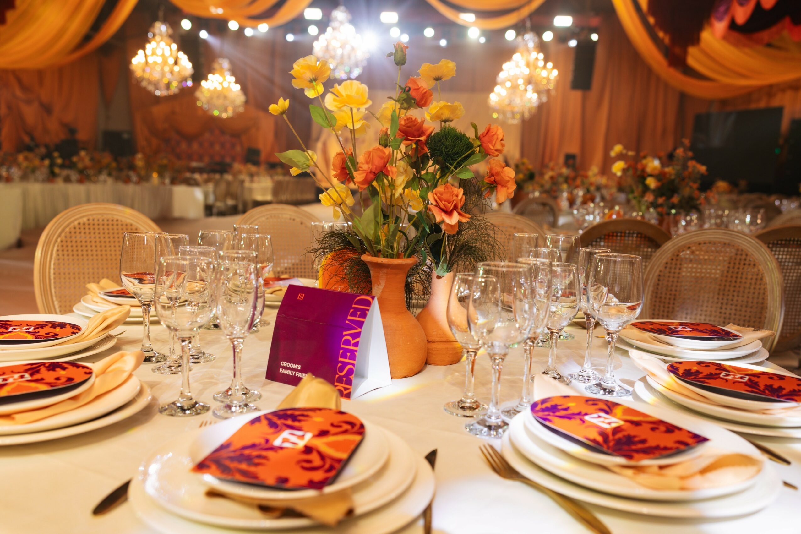 Elegant banquet table with floral centerpiece, set with plates, glasses, and napkins in a decorated event hall.