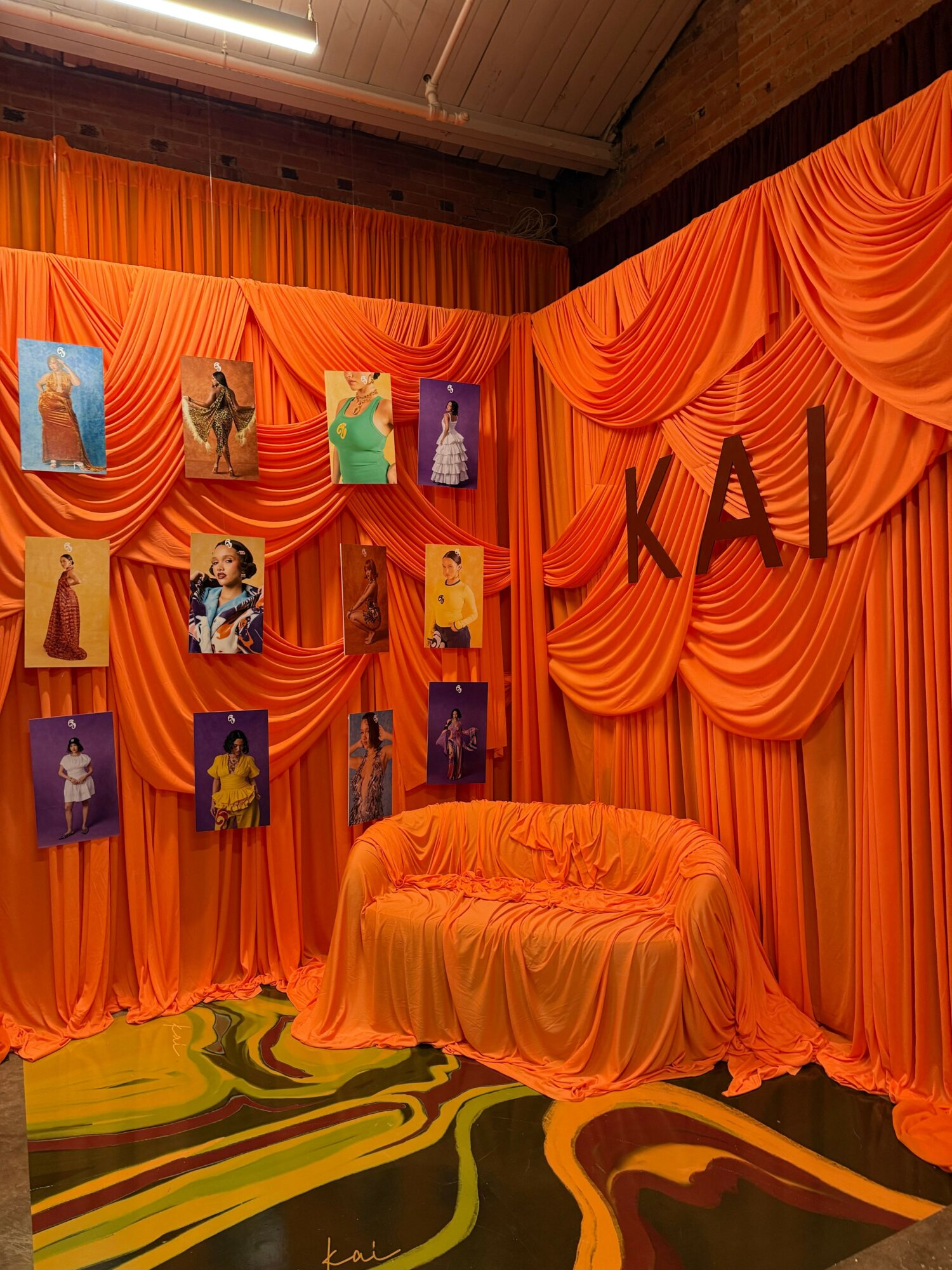 Orange fabric drapes and cushions with colorful artwork on the wall, and a vibrant abstract mural in the background.