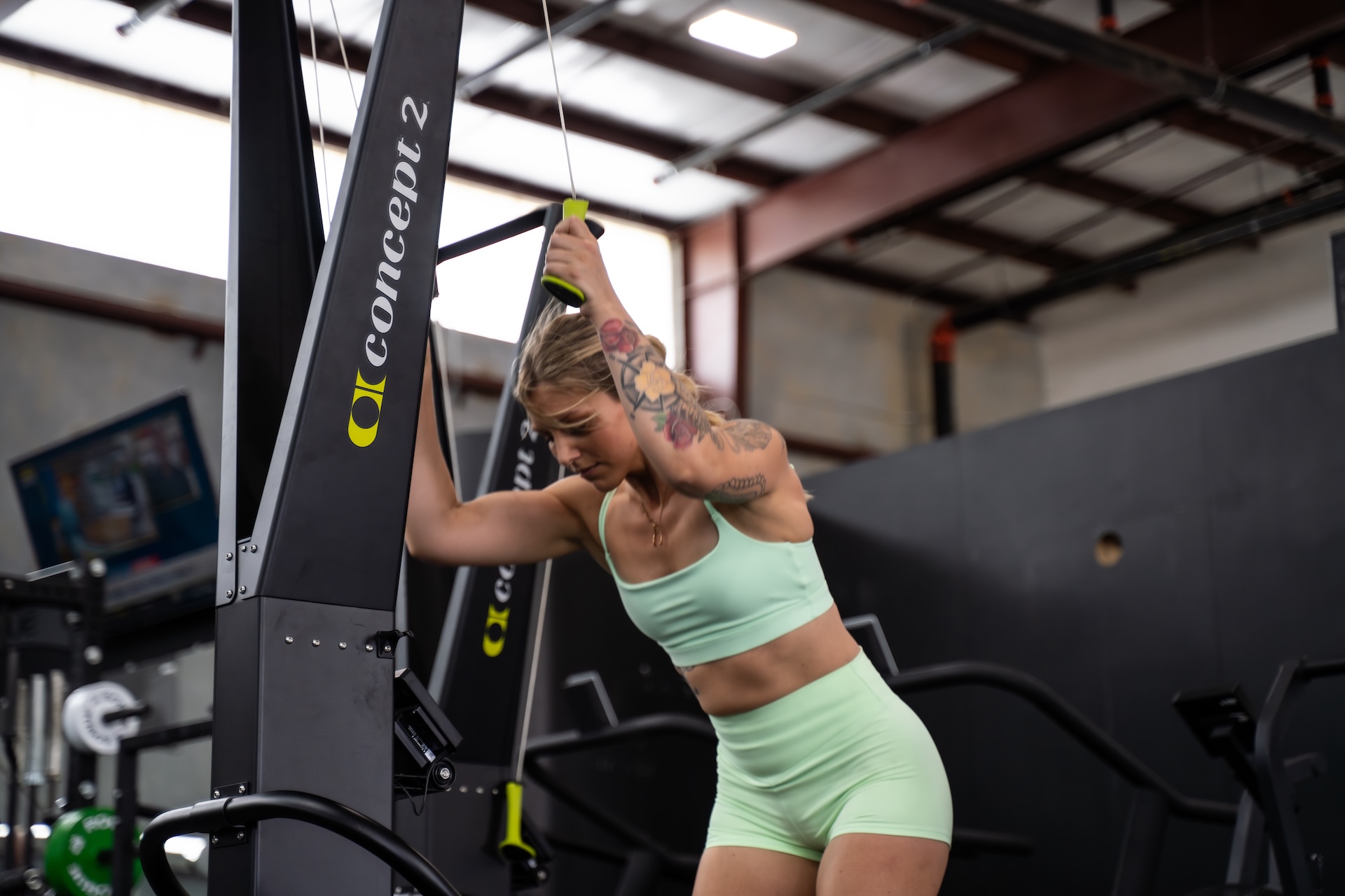 Woman exercising on a suspension trainer in a gym, wearing a light green sports bra and shorts, smiling.