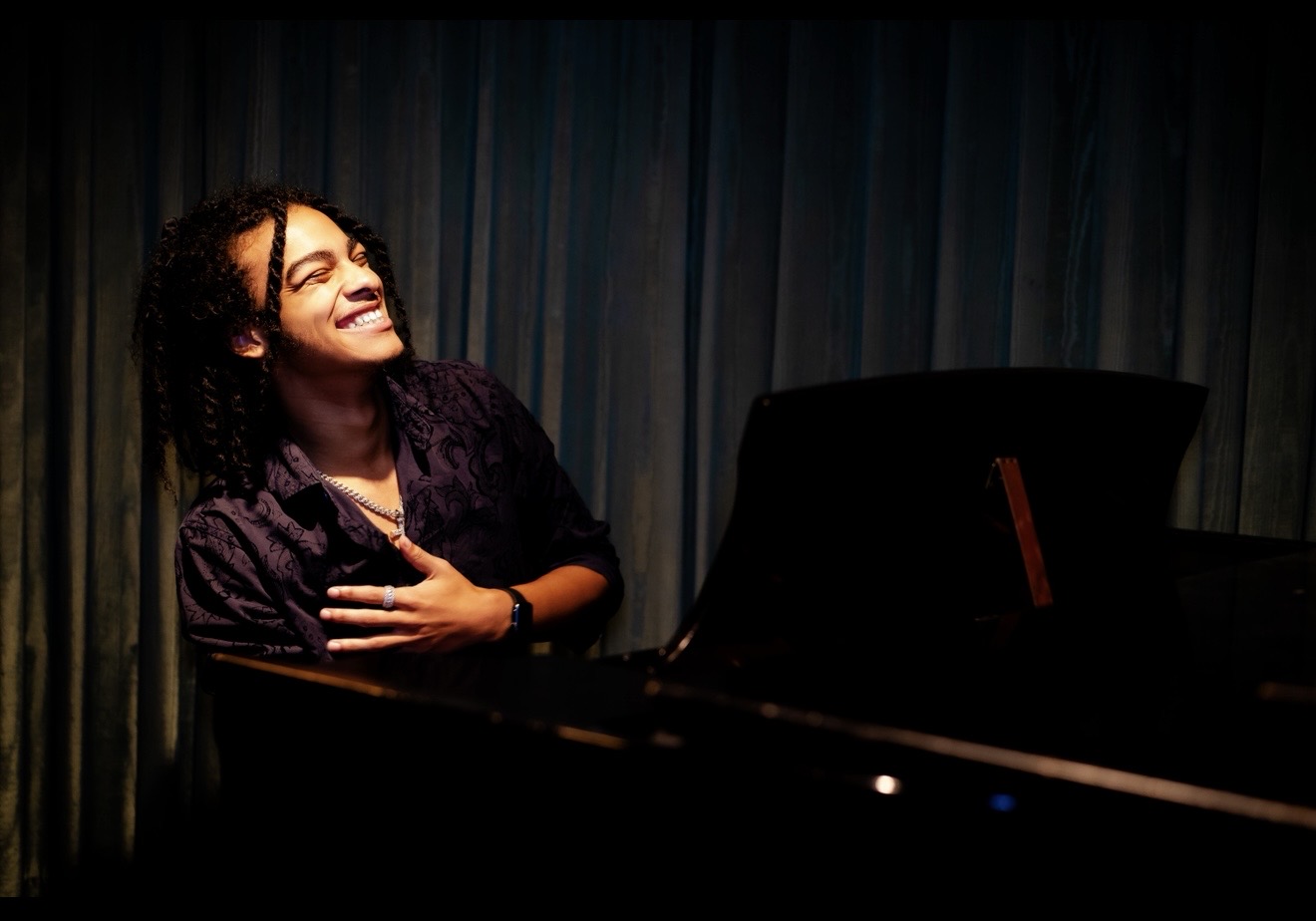 Woman smiling and laughing, sitting at a piano with a dark background.