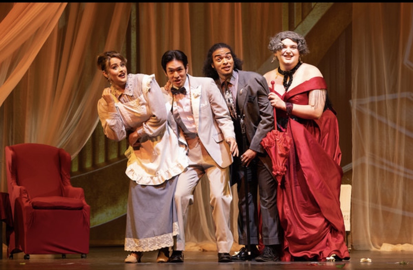 Four women in vintage costumes stand on stage with a red chair and curtain backdrop.