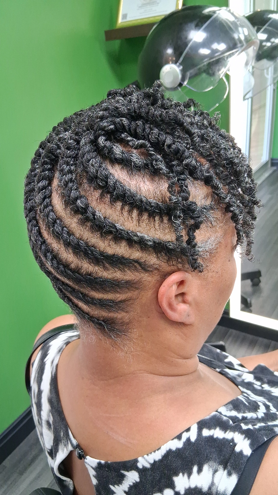 Side view of a person with tightly coiled, styled hair, and a green wall in the background.
