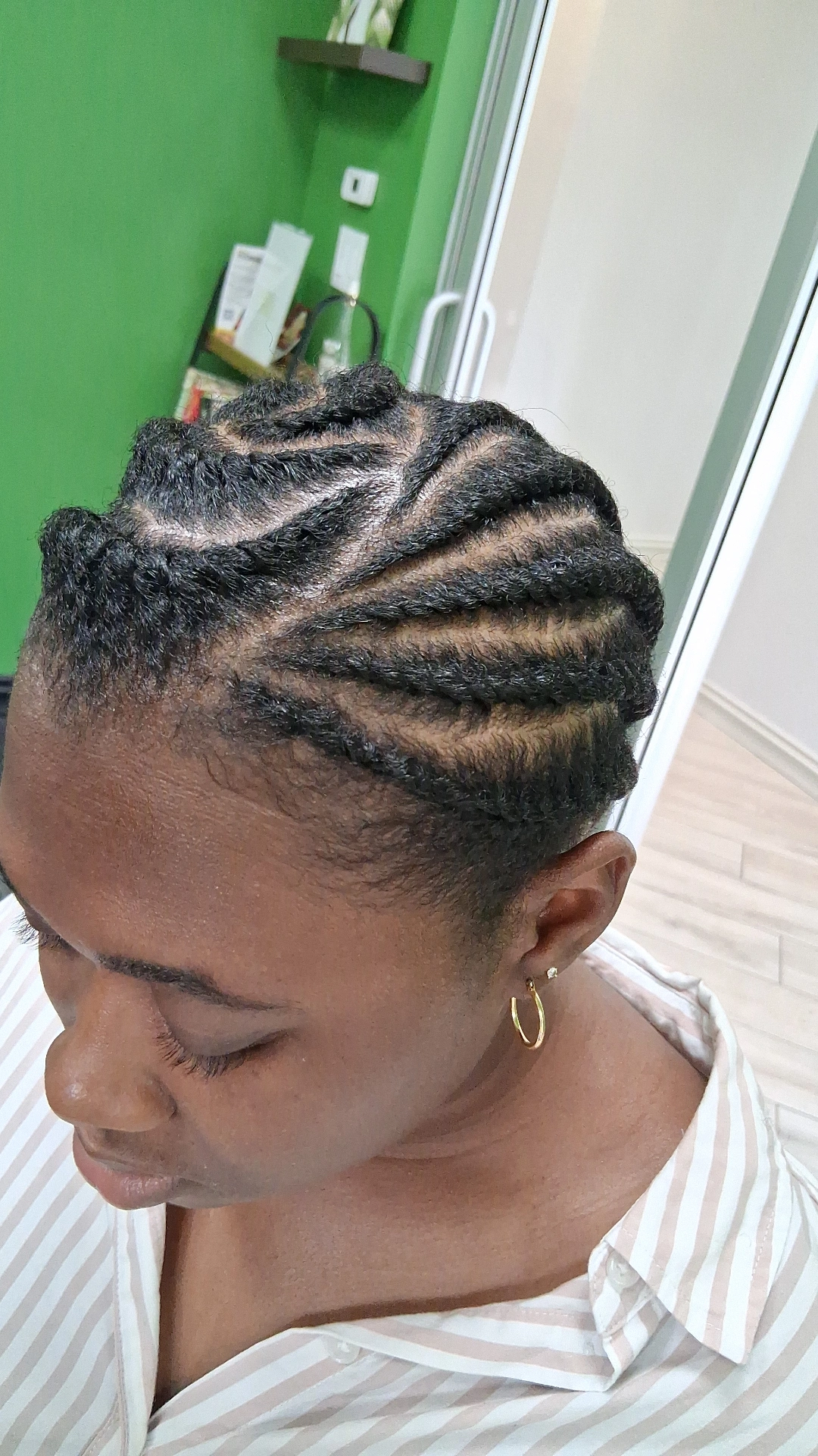 Woman with braided hairstyle, wearing a striped shirt and hoop earrings, in a room with green wall and white door.