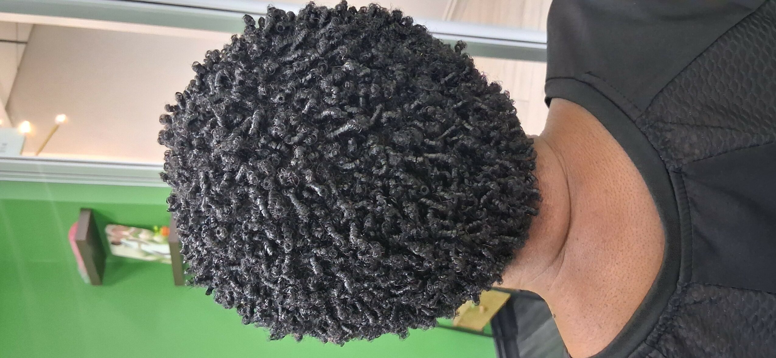Close-up of a person's head with curly black hair, viewed from the side, with a green background.