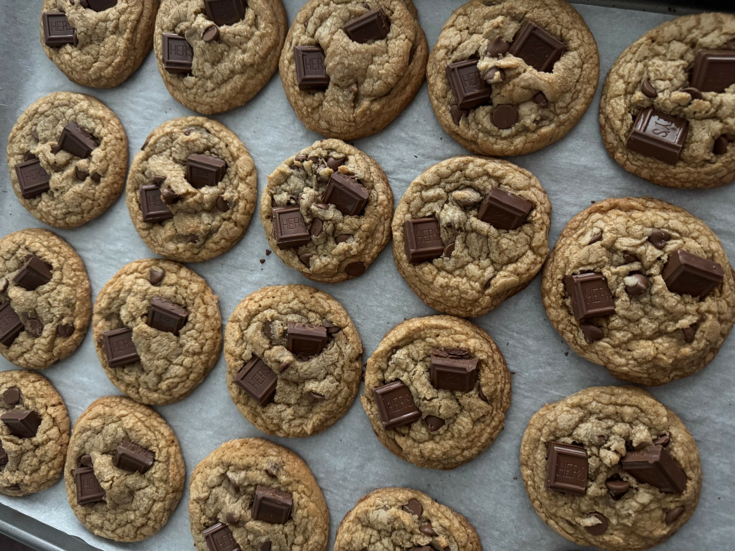 Chocolate chip cookies with chunks of chocolate on a light surface, arranged in rows.
