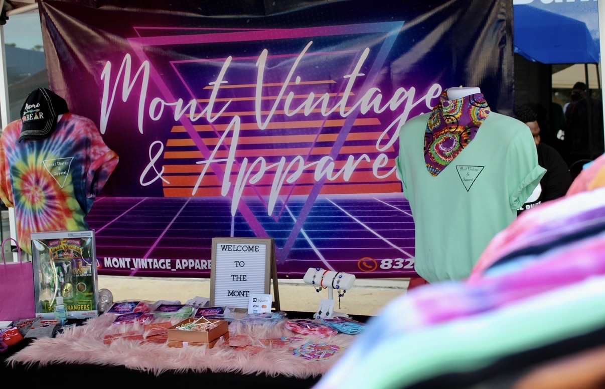 Display booth with clothing and accessories in front of a pink and purple banner reading 'Mont Vintage & Apparel'.