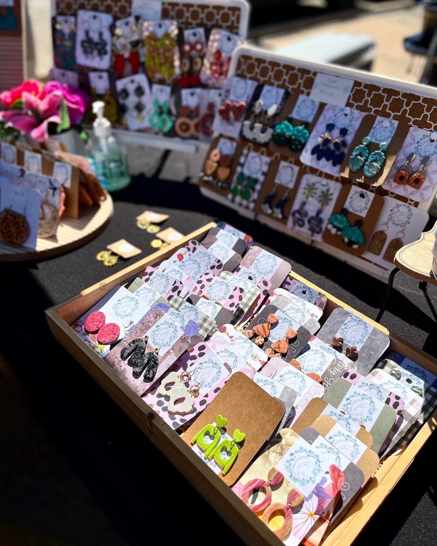 Display of colorful handmade earrings and accessories on boards and in a box at an outdoor market stall.