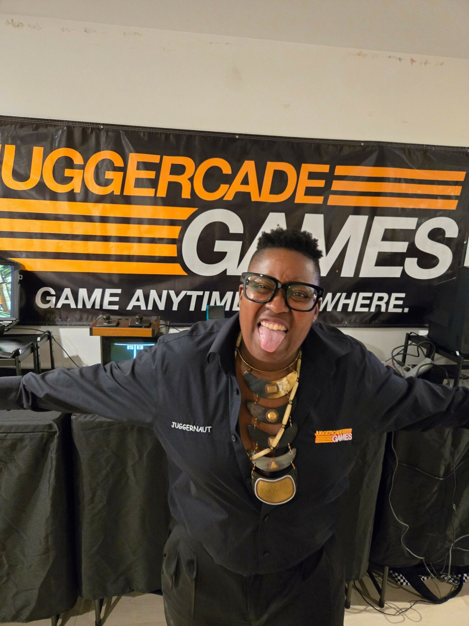Man with glasses and a beard wearing a black jacket standing in front of a banner at an arcade event.