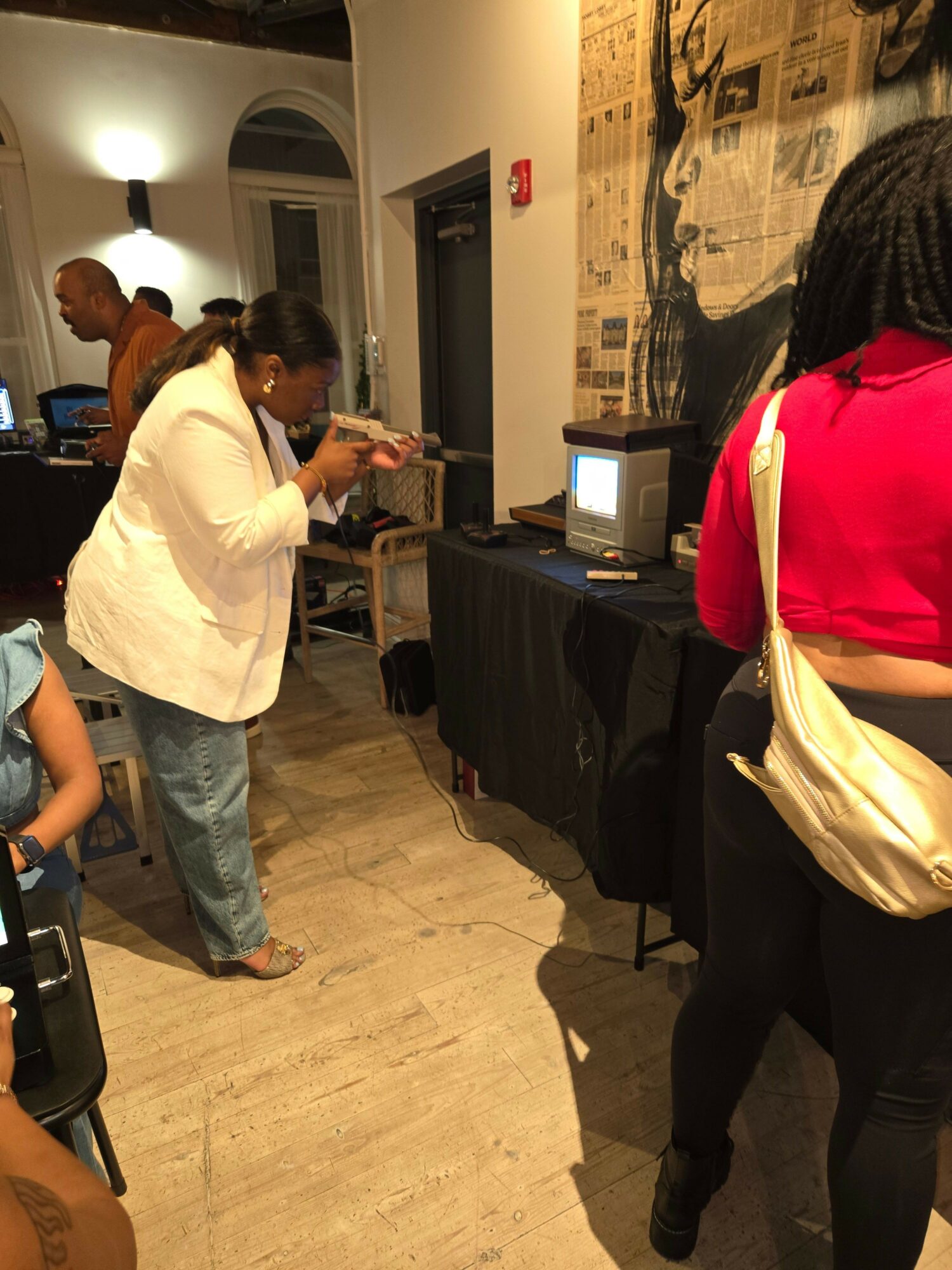 Person in white shirt and jeans interacts with a child in a room with computers and a black table.