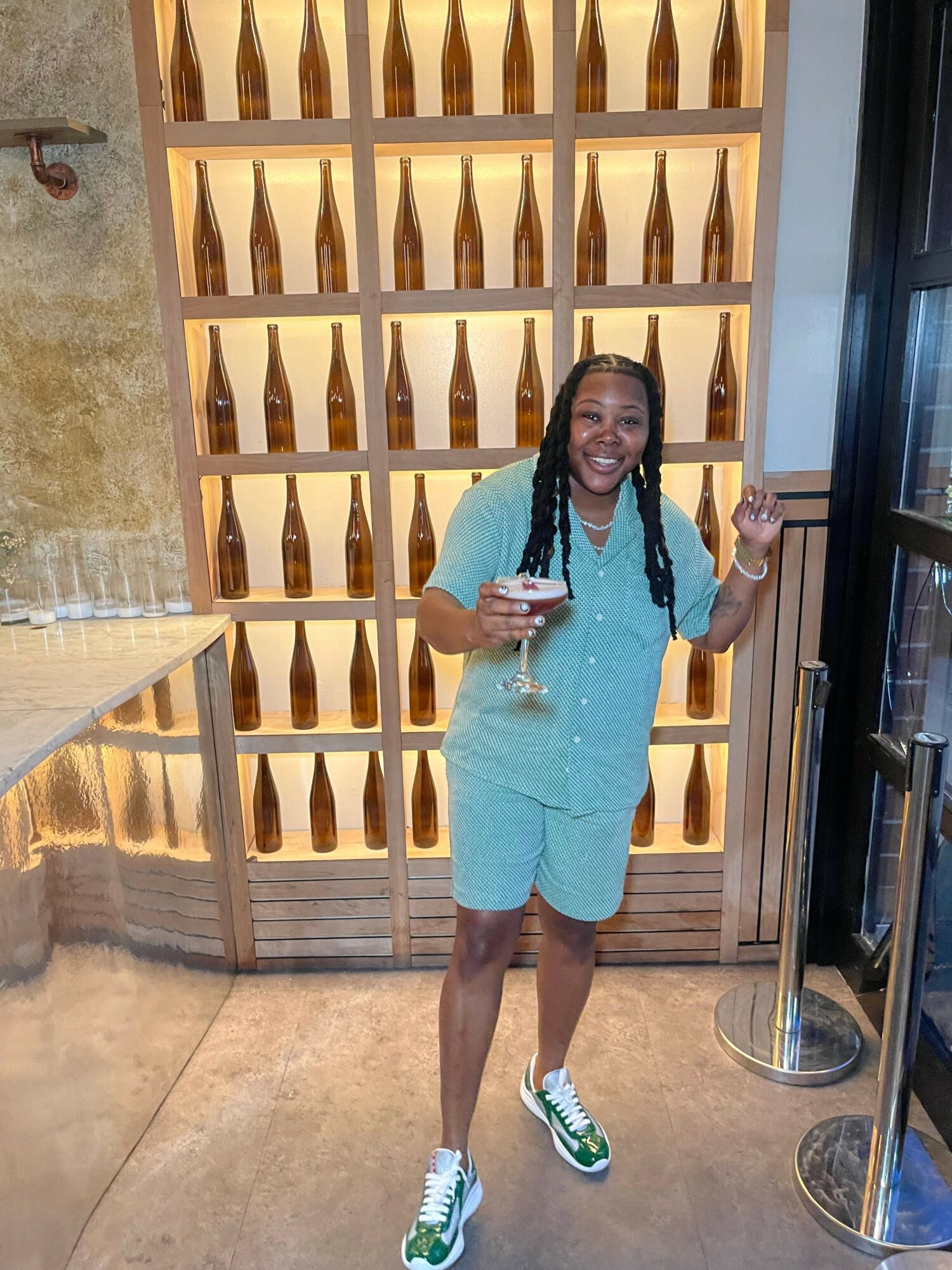 Woman in light blue dress and sneakers taking a selfie in a modern interior with wooden wall decor.