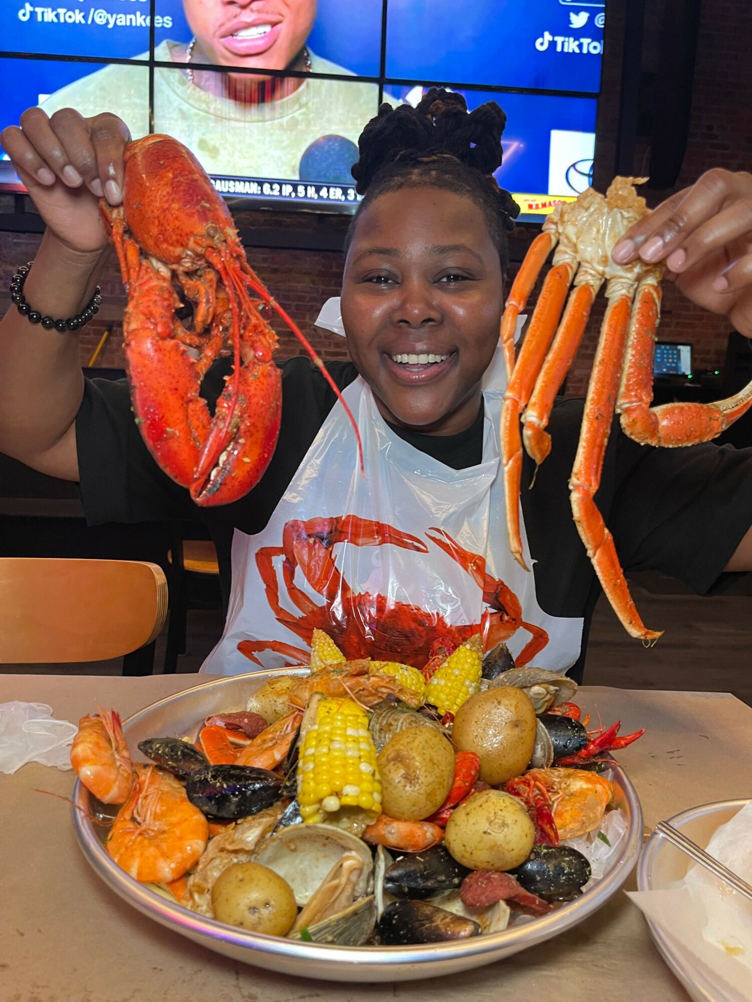 Person holding a cooked lobster and crab, smiling, with a large seafood platter on the table.
