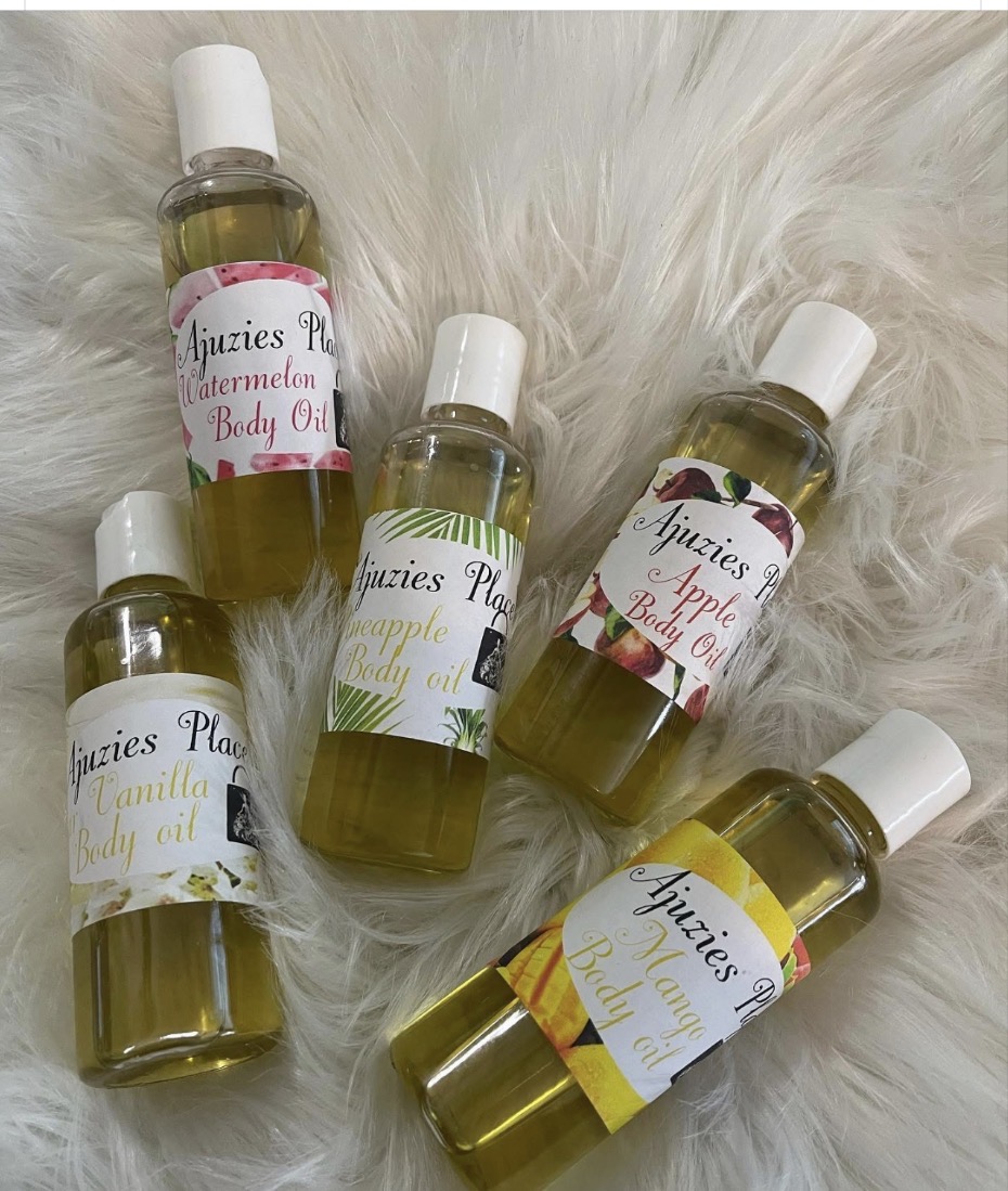 Five bottles of body oil with colorful labels on a white furry surface.