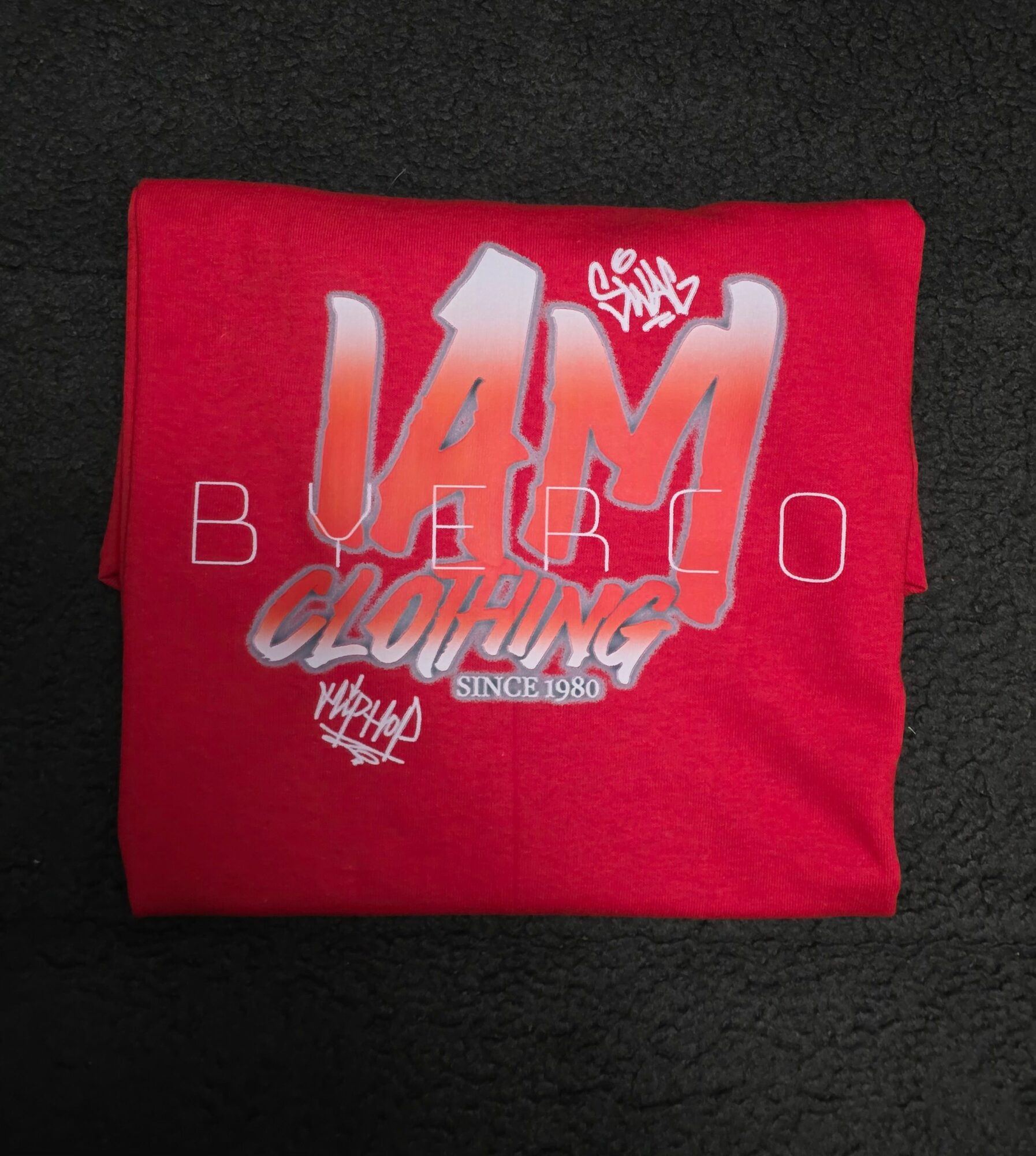 Red fabric with white and silver text and graphics, partially folded, on a black background.