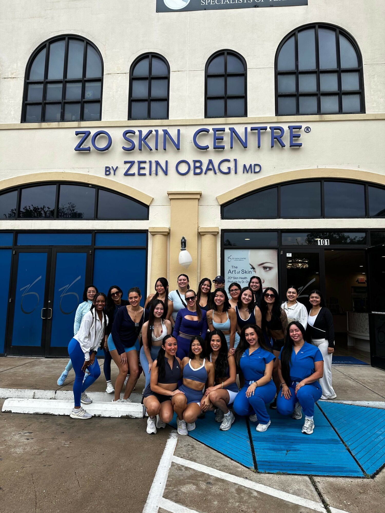 Group of people sitting and standing outside a building with a sign reading 'ZOE SKIN CENTRE' and 'ZEIN OBAGI'.