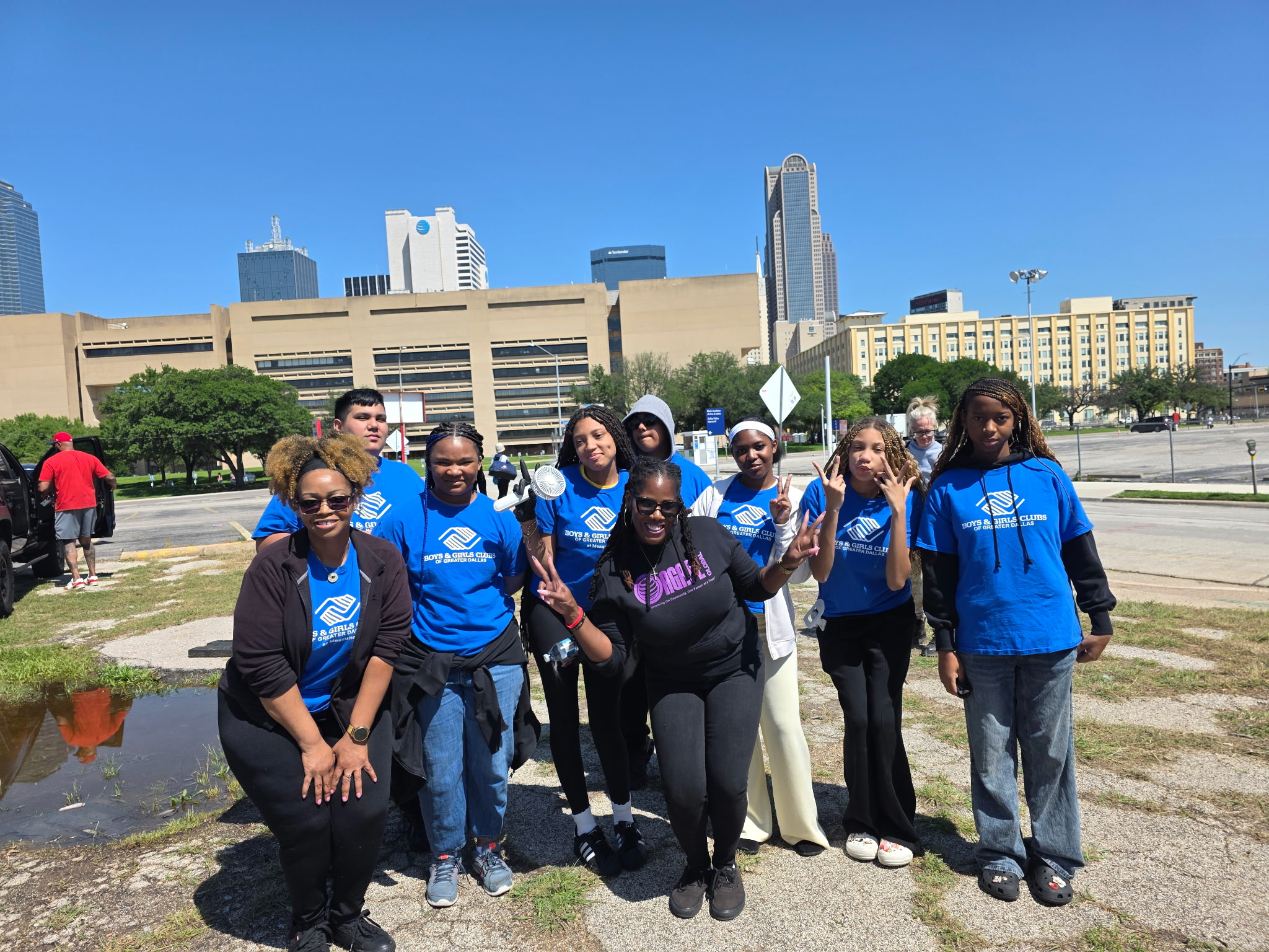 Group of eight people standing outdoors in front of a city skyline, some wearing blue shirts, smiling.
