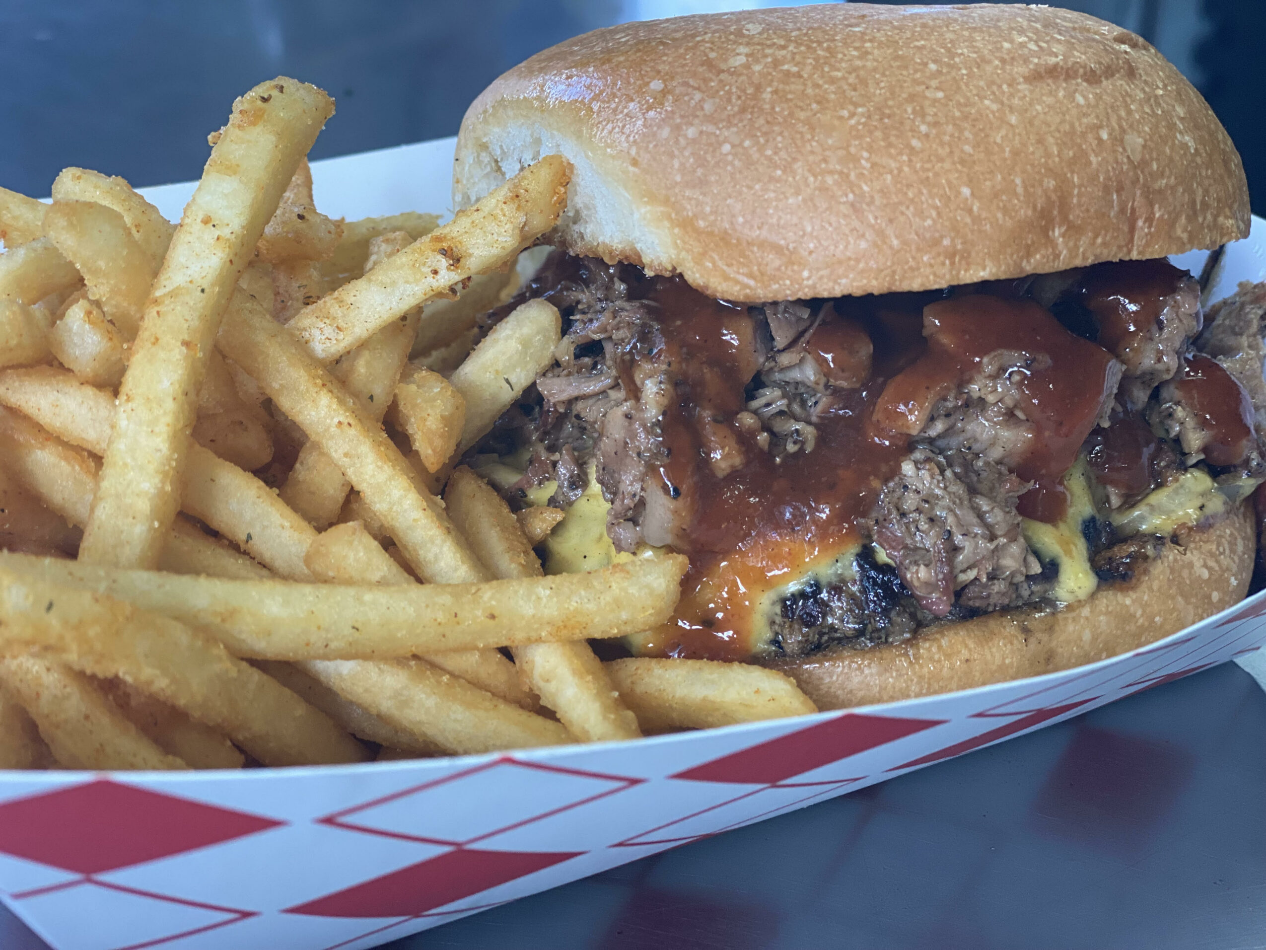 A cheeseburger with fries on a tray, with a bun, beef patty, cheese, lettuce, tomato, and sauce.
