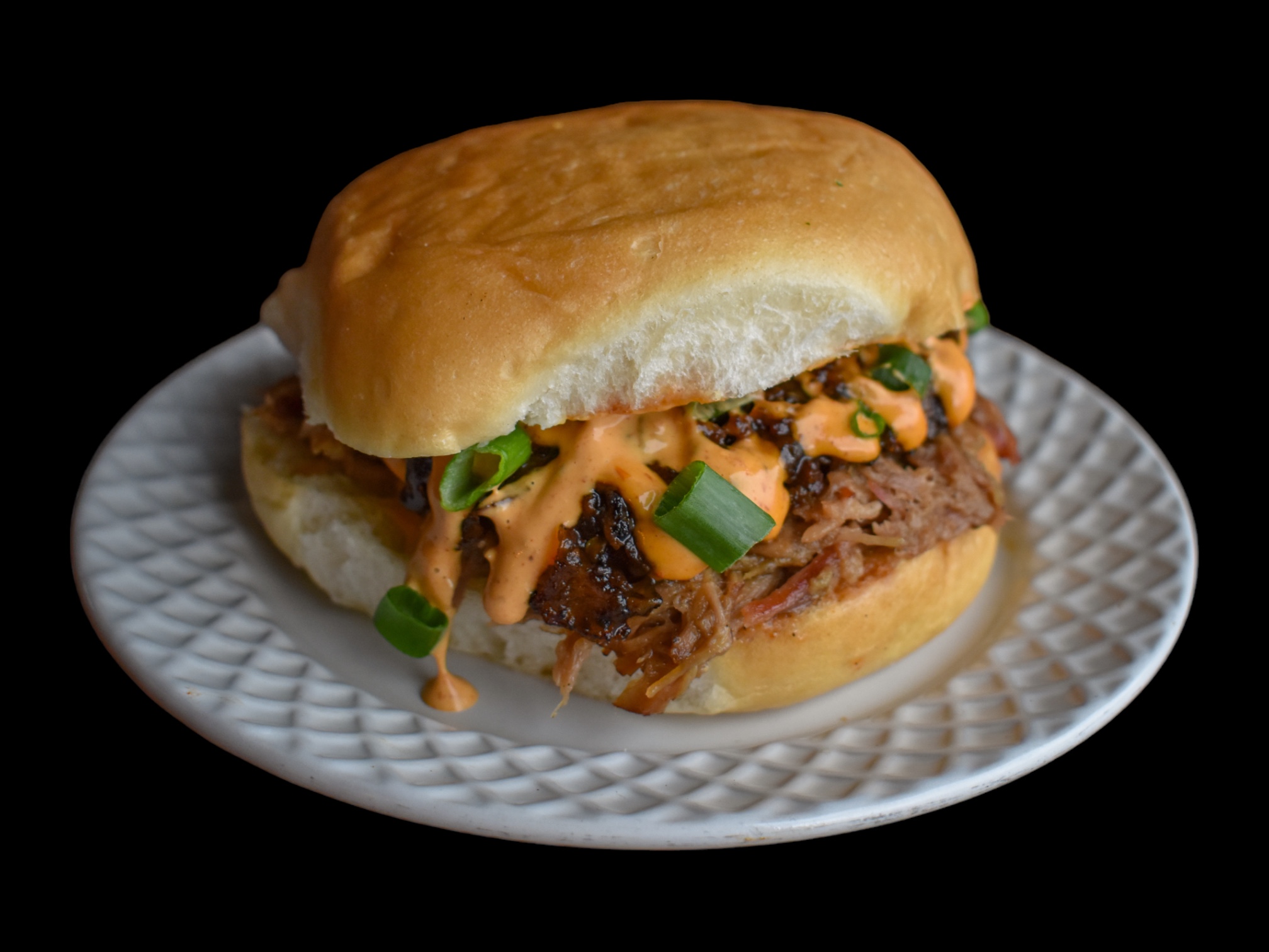 Beef sandwich with sauce and green onions on a white plate against a black background.