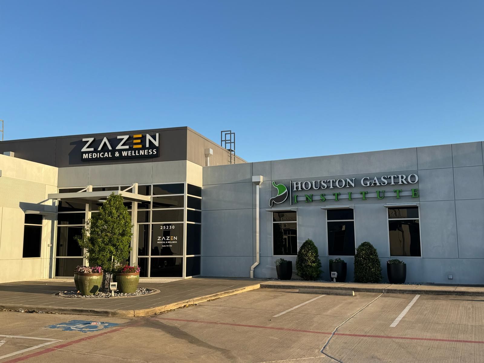 Buildings with signs for Zazen Medical & Wellness and Houston Gastro, parking lot in foreground, clear sky.