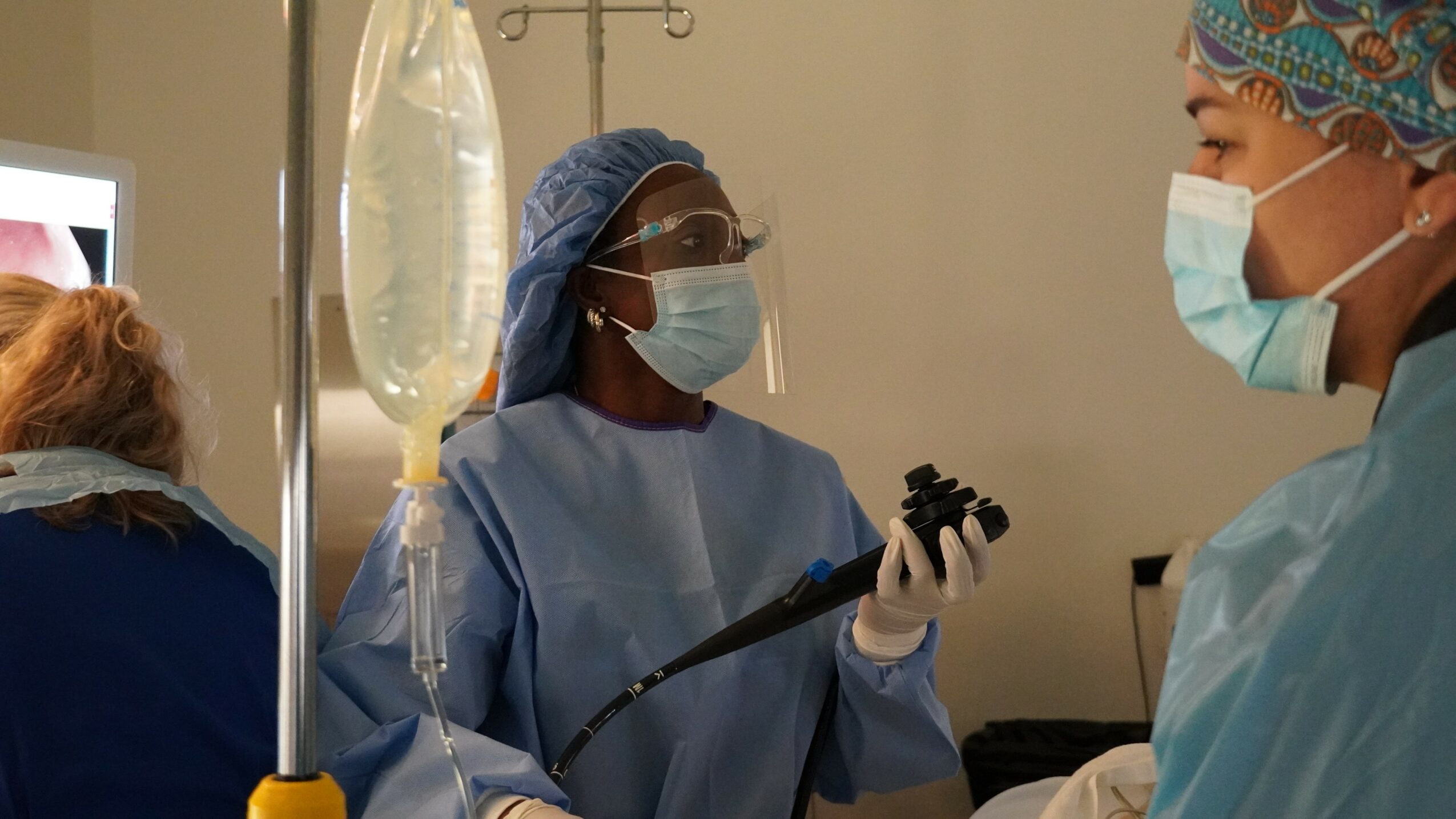 Medical professionals in scrubs and masks in a clinical setting, with one holding a medical instrument.