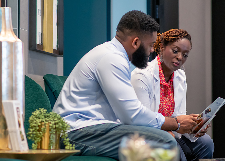 Two people sitting on a green bench, looking at a tablet, in a modern indoor setting.
