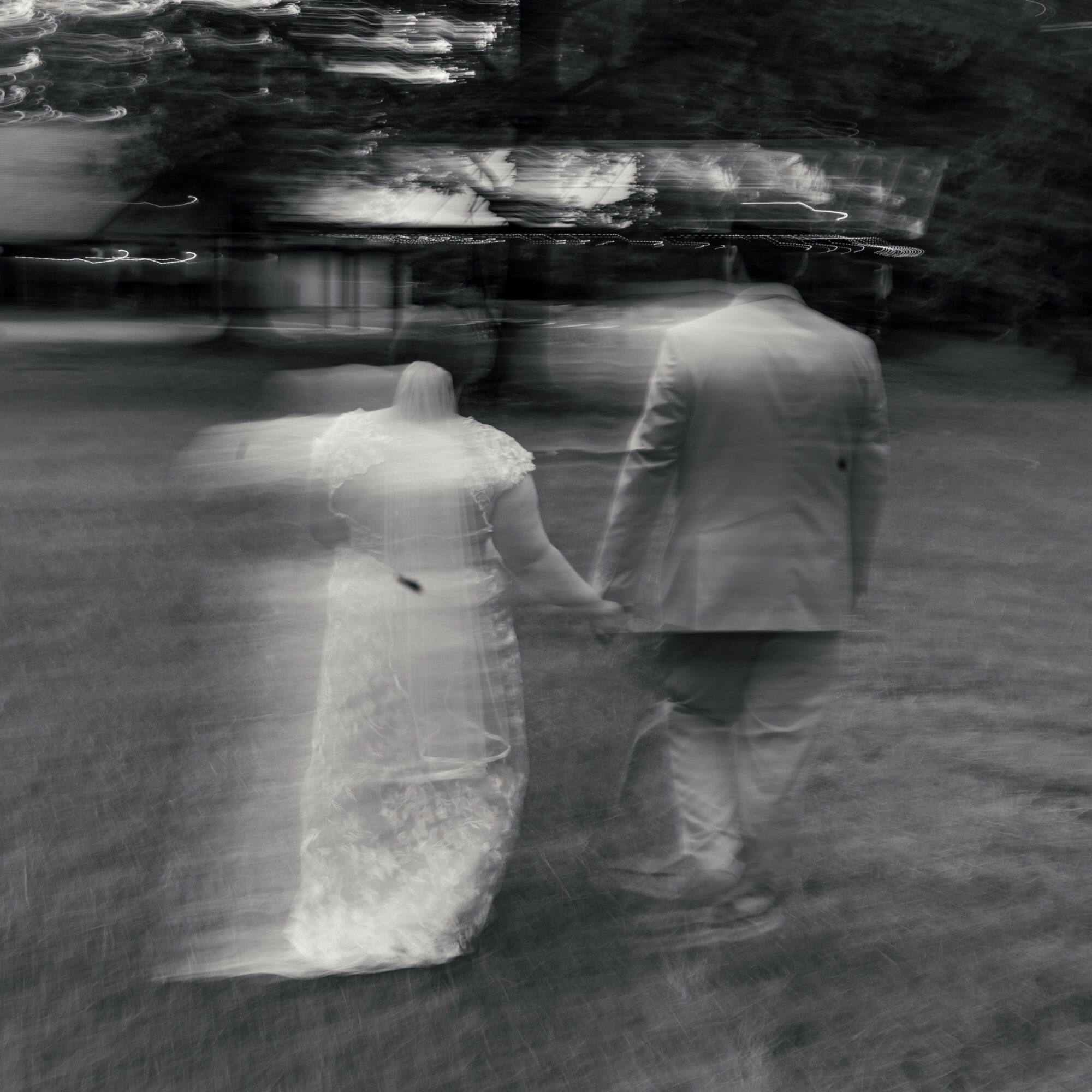 Two people, a man and a woman, walk hand in hand outdoors, with blurred background, in black and white.