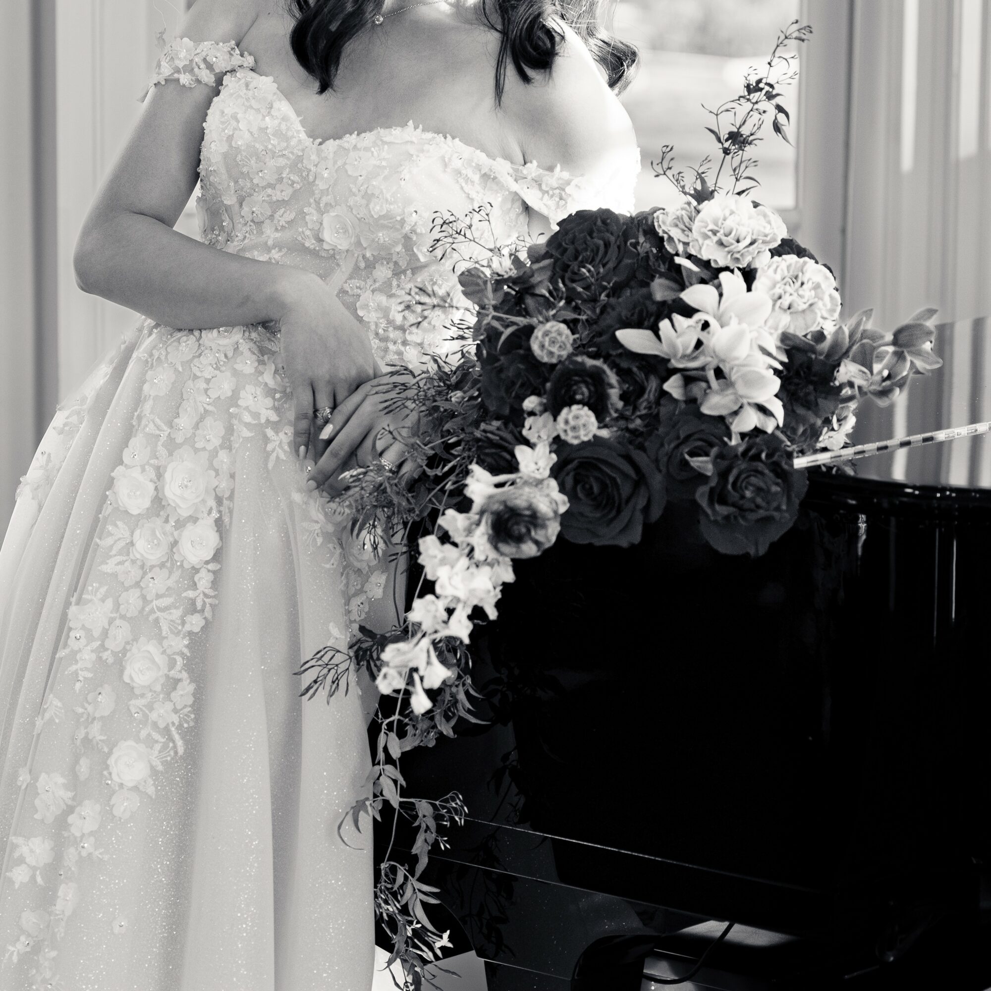 Woman in wedding dress holding a large bouquet of flowers, standing near a piano, with a window in the background.