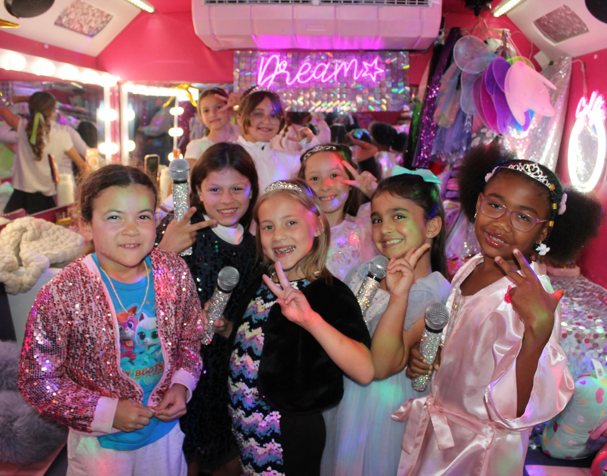 Group of children in a colorful room with a neon sign that says 'Dream,' smiling and posing for the photo.