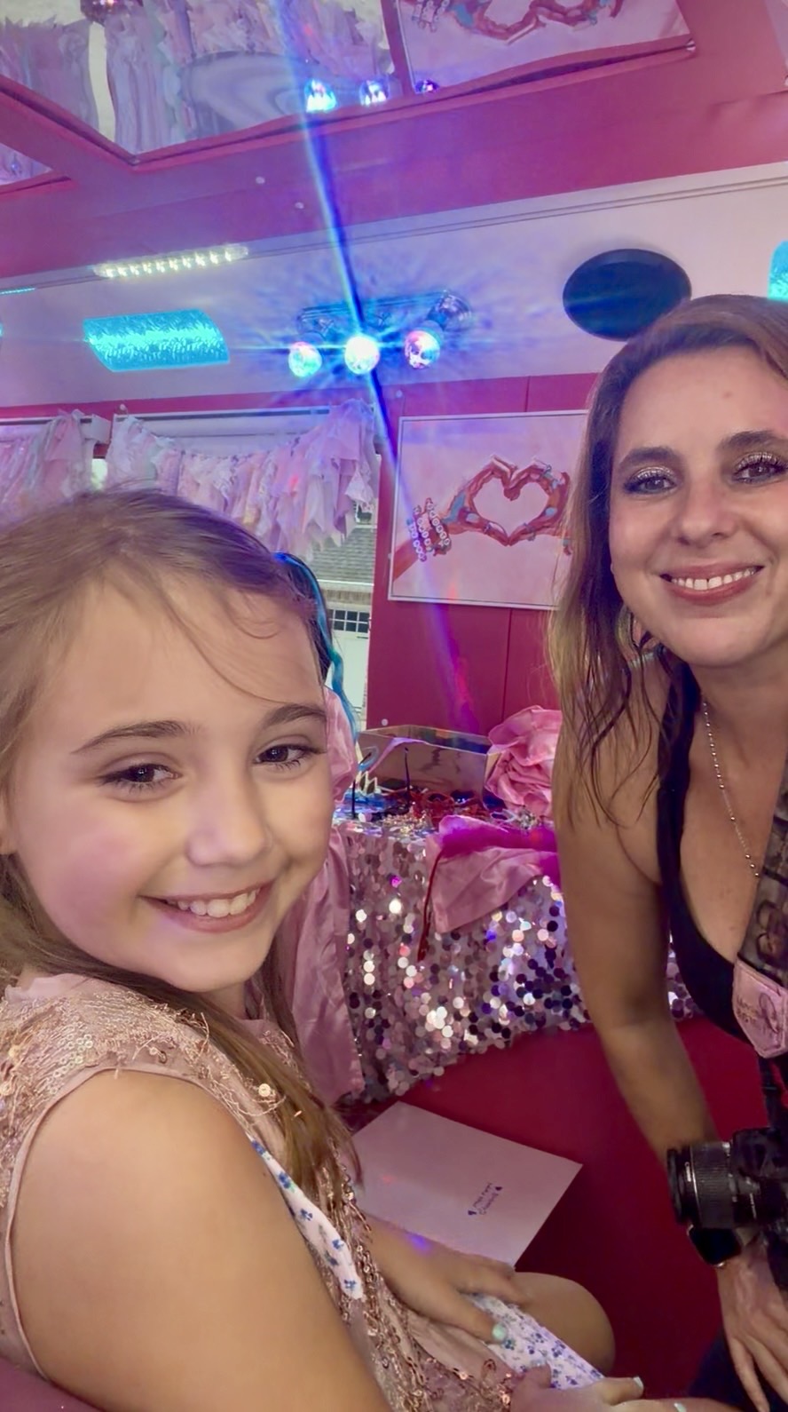 Two smiling females at a decorated party table with colorful lights and drawings in the background.