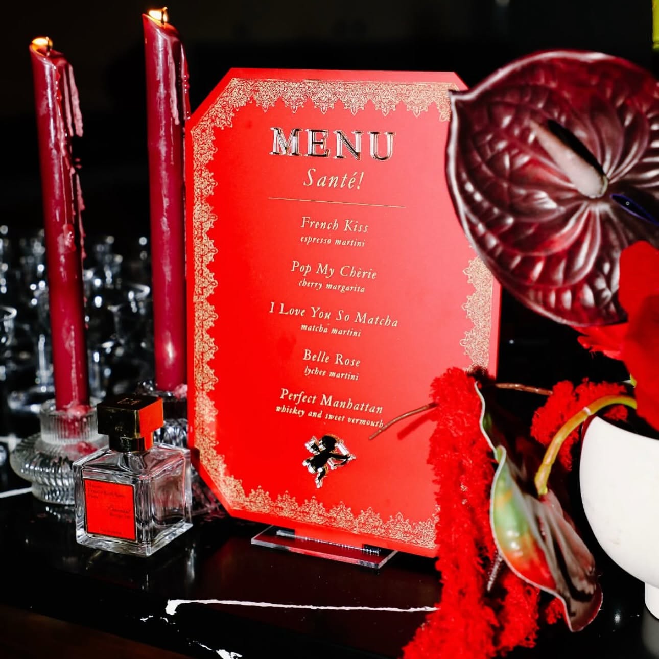 Valentine's Day themed menu with red candles, flowers, and perfume bottles on a dark surface.