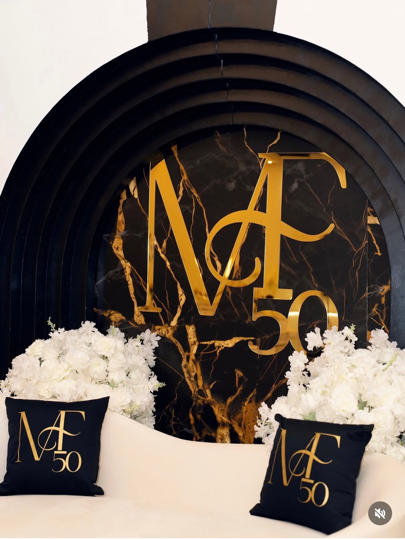 Decorative black and gold backdrop with white flowers and black pillows with gold lettering, celebrating 50 years.