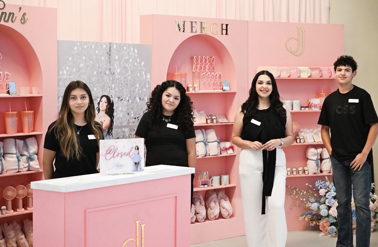 Four people stand behind a pink display counter in a store with pink shelves and decorative items.