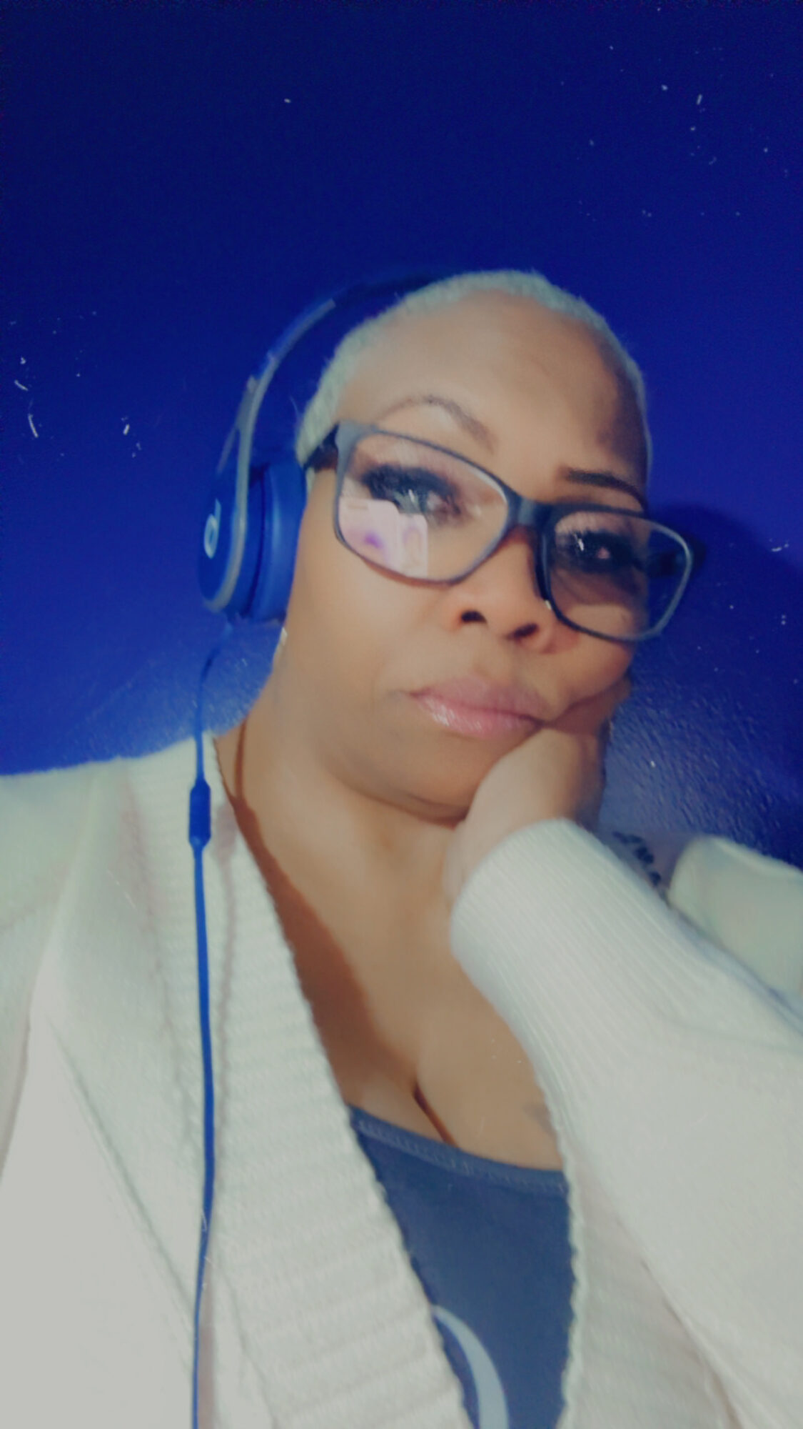Woman with glasses and headphones resting her chin on her hand, against a starry night sky background.