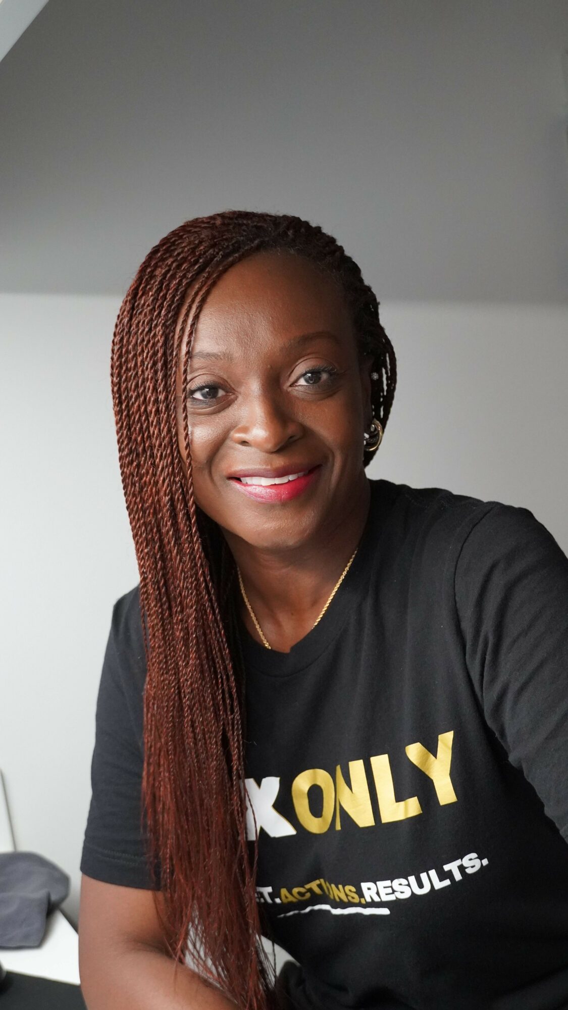 Woman with braided hair smiling, wearing a black shirt with text, against a plain background.