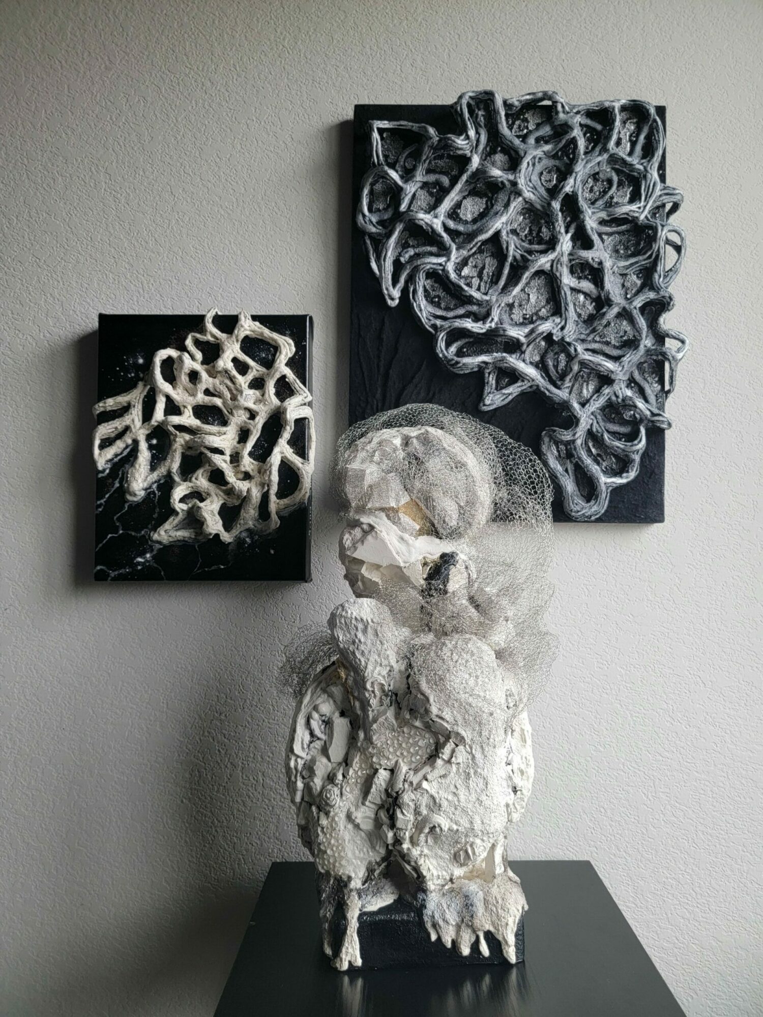 Two abstract sculptures with intricate, web-like structures on black bases, displayed on a light-colored wall.