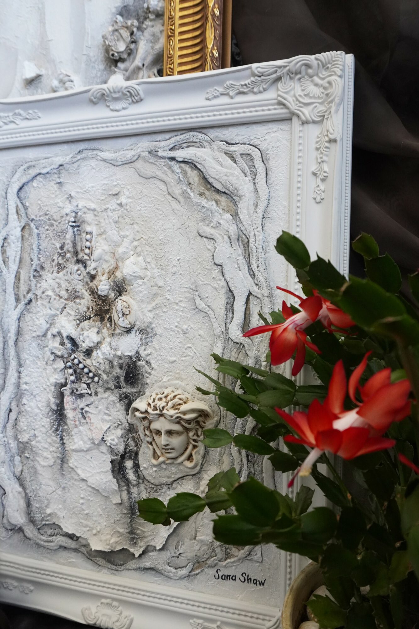 Decorative textured wall with a carved face sculpture and a plant with red flowers in front.
