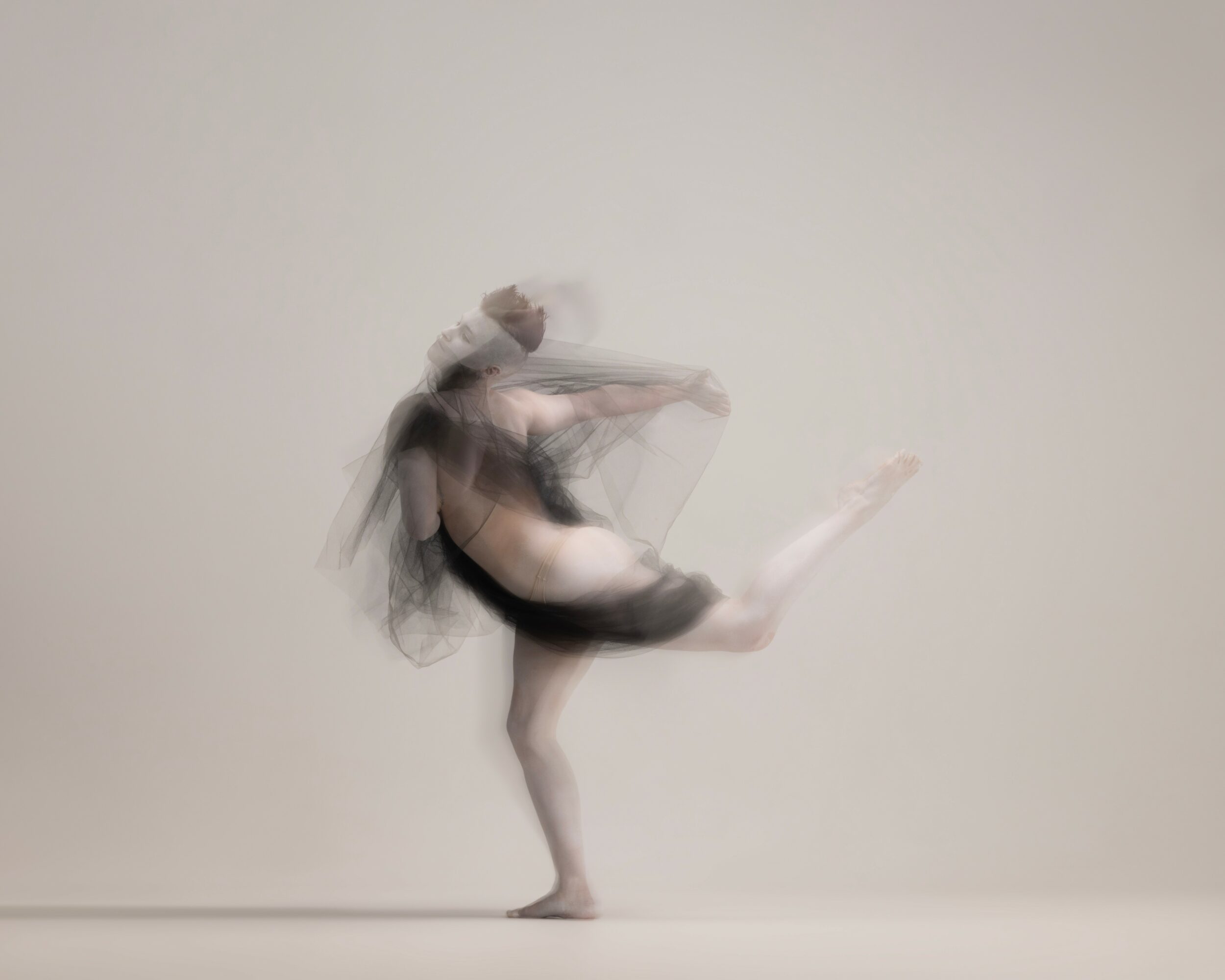 A dancer in motion, captured with motion blur, performing a high kick against a plain background.