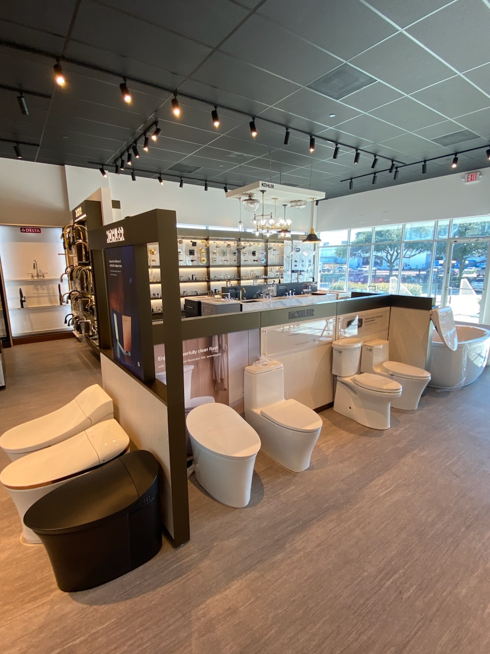 Showroom with toilets and bathroom fixtures near large windows, modern interior with ceiling lights and display shelves.