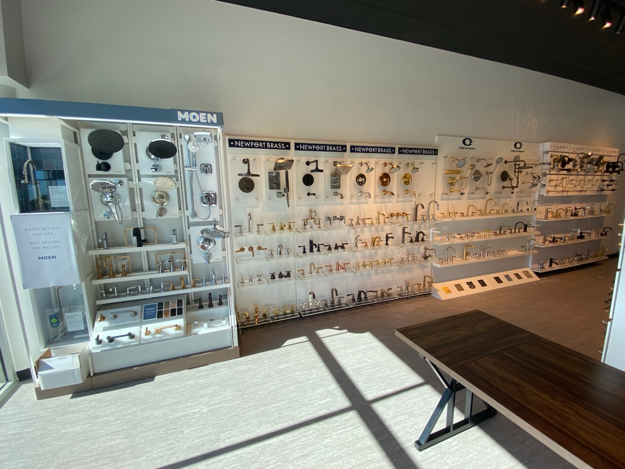 Display of various hardware and tools on white shelves and wall panels in a store, with a wooden table in the foreground.
