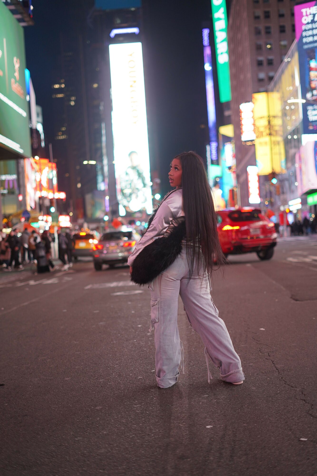 Person standing on city street at night with bright lights and signs in the background.