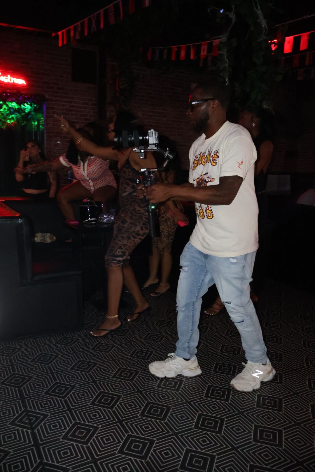 Group of people dancing in a dimly lit nightclub with colorful lights, some holding drinks.