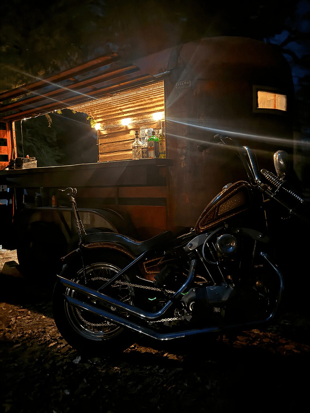 Motorcycle parked next to a wooden cart with a lit interior, outdoors at night.