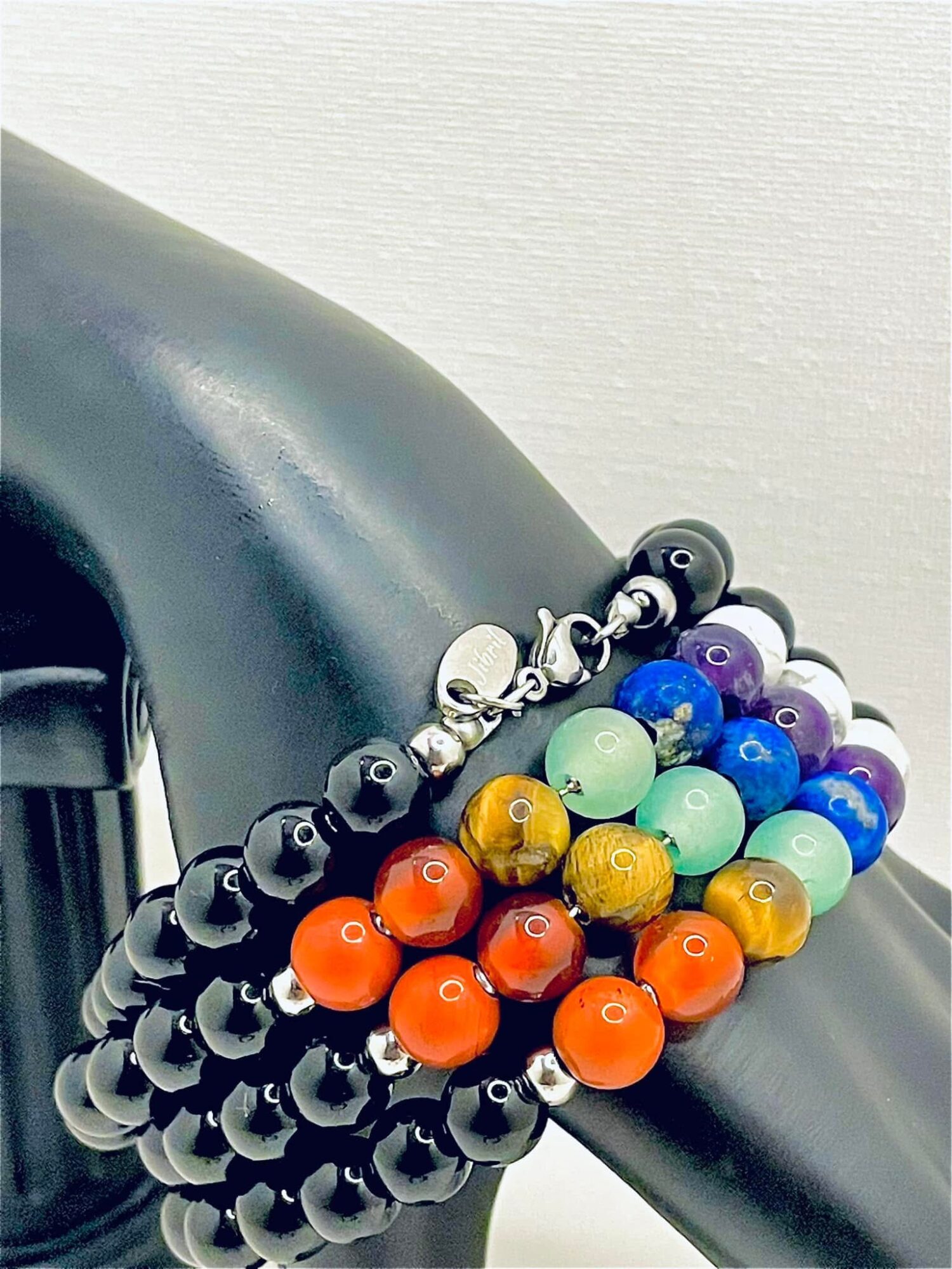 Colorful beaded bracelet with black, white, blue, purple, yellow, and orange beads, draped over a black curved surface.
