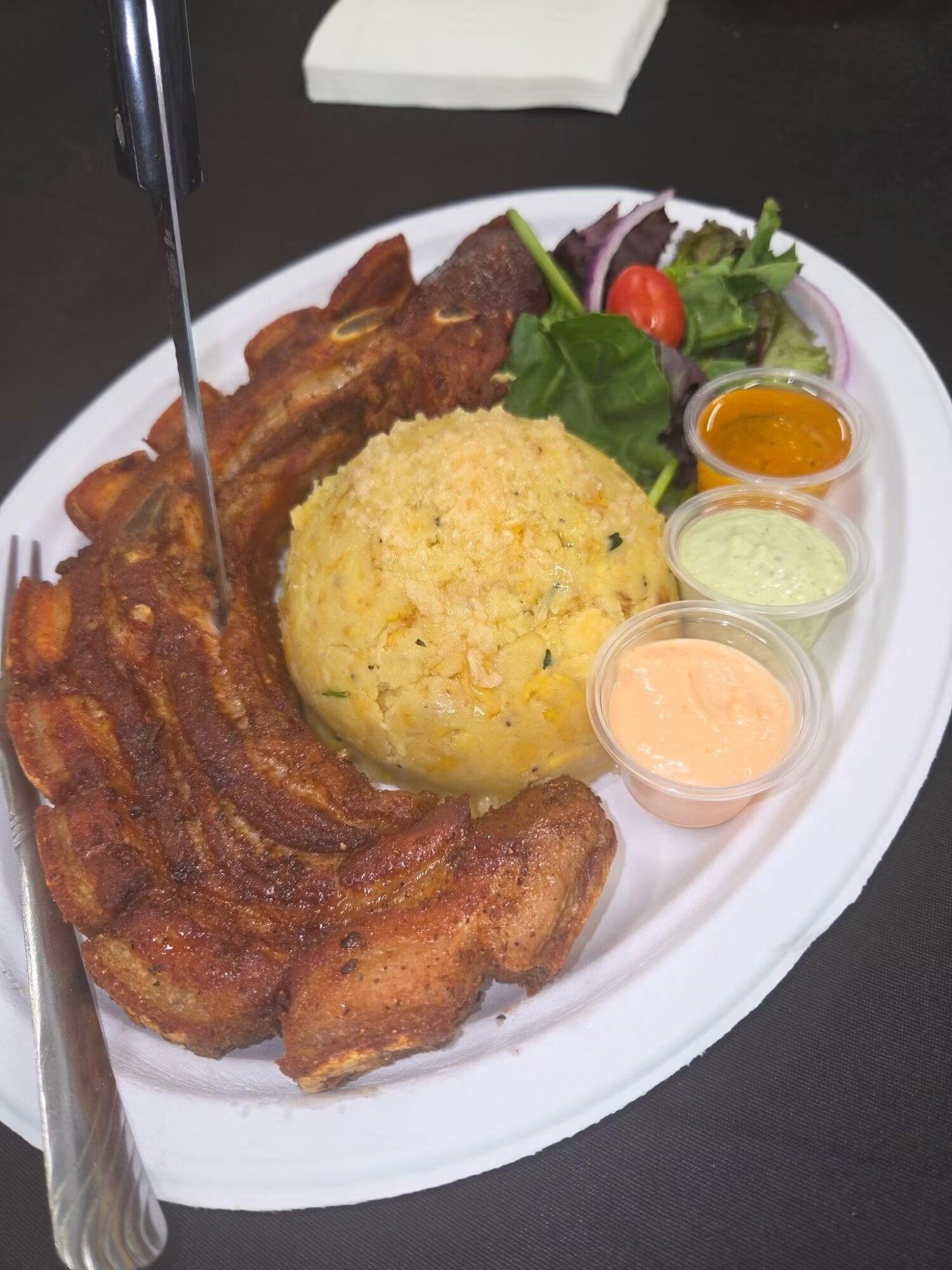 Fried chicken, rice, salad, and three small sauces on a white oval plate.